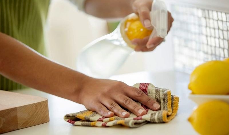 cropped image of a woman wiping a surface with a cloth and a spray bottle