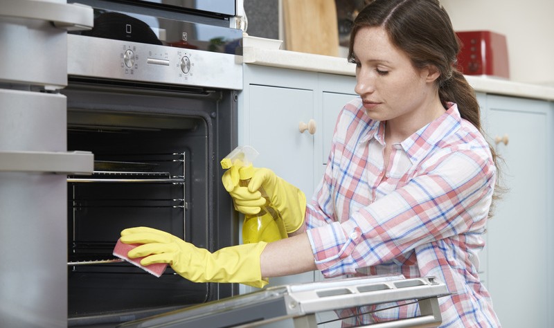 young woman wiping oven grills with a sponge