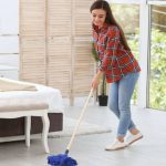 Woman in check shirt and blue jeans scrubbing inside a room