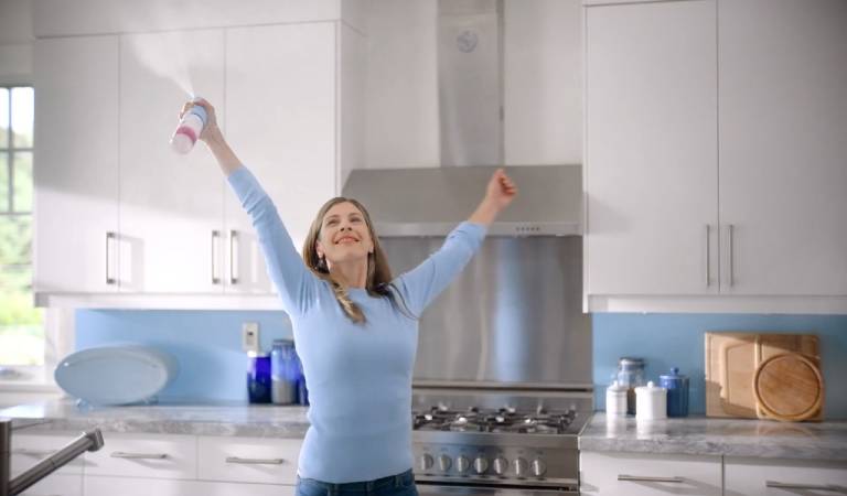 Woman in blue t-shirt holding spray bottle inside a kitchen