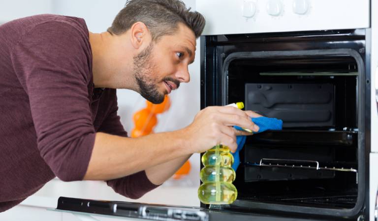Man in brown t-shirt holding spray bottle and spraying on oven