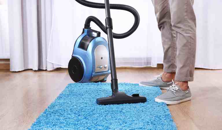 Leg of a man and a vacuum cleaner on blue carpet inside a living room.
