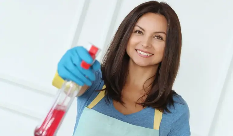 Cleaning lady in blue gloves holding a bottle in her hand.