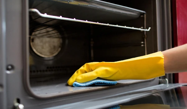 hand in rubber glove with rag cleaning oven at home kitchen