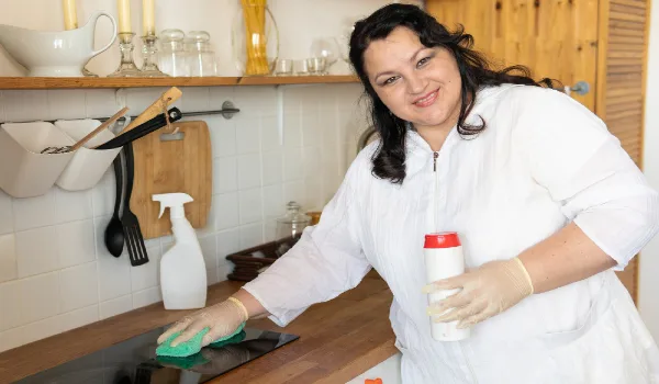 A woman with a rag cleans and washes in the kitchen