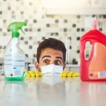 Man bottles and products by kitchen counter for cleaning peeking and cleaner with chemical liquid container spray